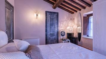 A bedroom with a bed, a chair, a door, and a wall-mounted light fixture.