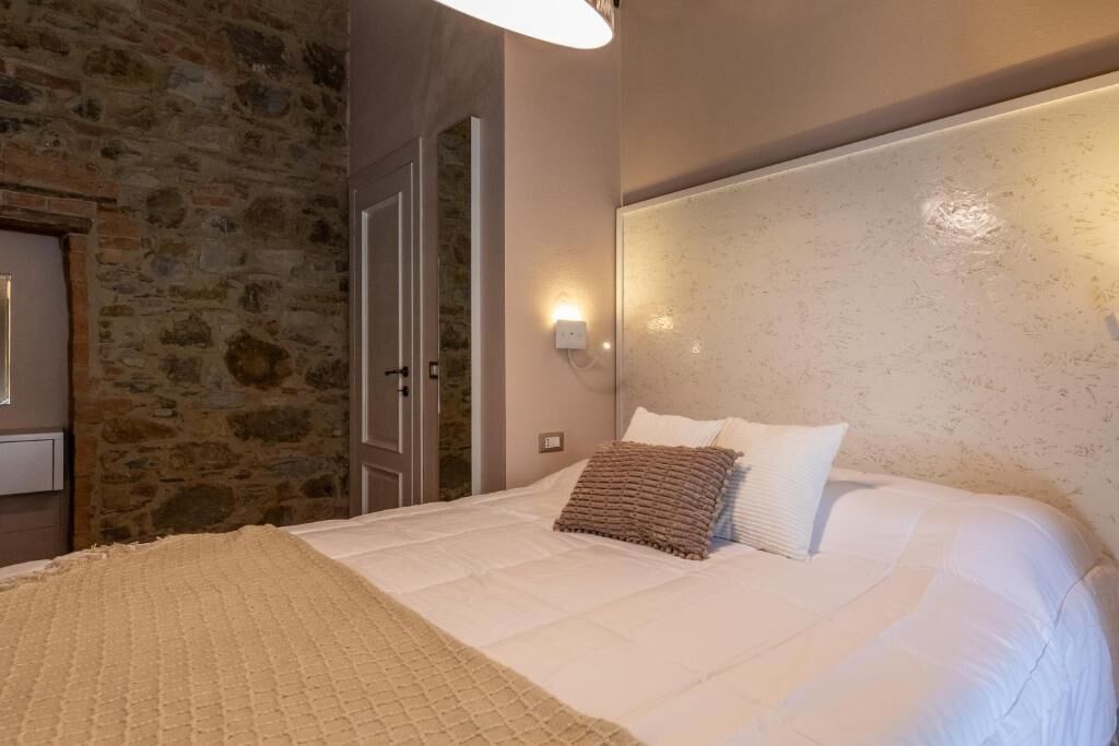 A bedroom with a stone wall, a bed with white bedding, a headboard with wall-mounted lights, and a door.