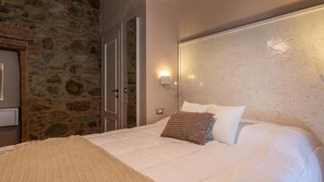 A bedroom with a stone wall, a bed with white bedding, a headboard with wall-mounted lights, and a door.