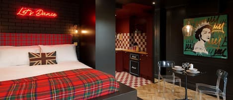 A hotel room with a bed, a neon sign, a checkered floor, a table with chairs, and a painting on the wall.