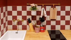 A kitchen with a white sink, a black induction cooktop, a red and white checkered backsplash, and a wooden countertop. - Guestready - Camden Studios (London)