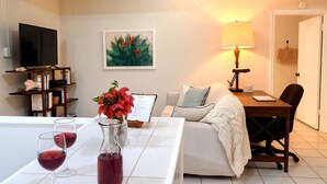 Een woonkamer met een bank, een salontafel met wijnglazen, een televisie, een boekenkast, een schilderij en een lamp.