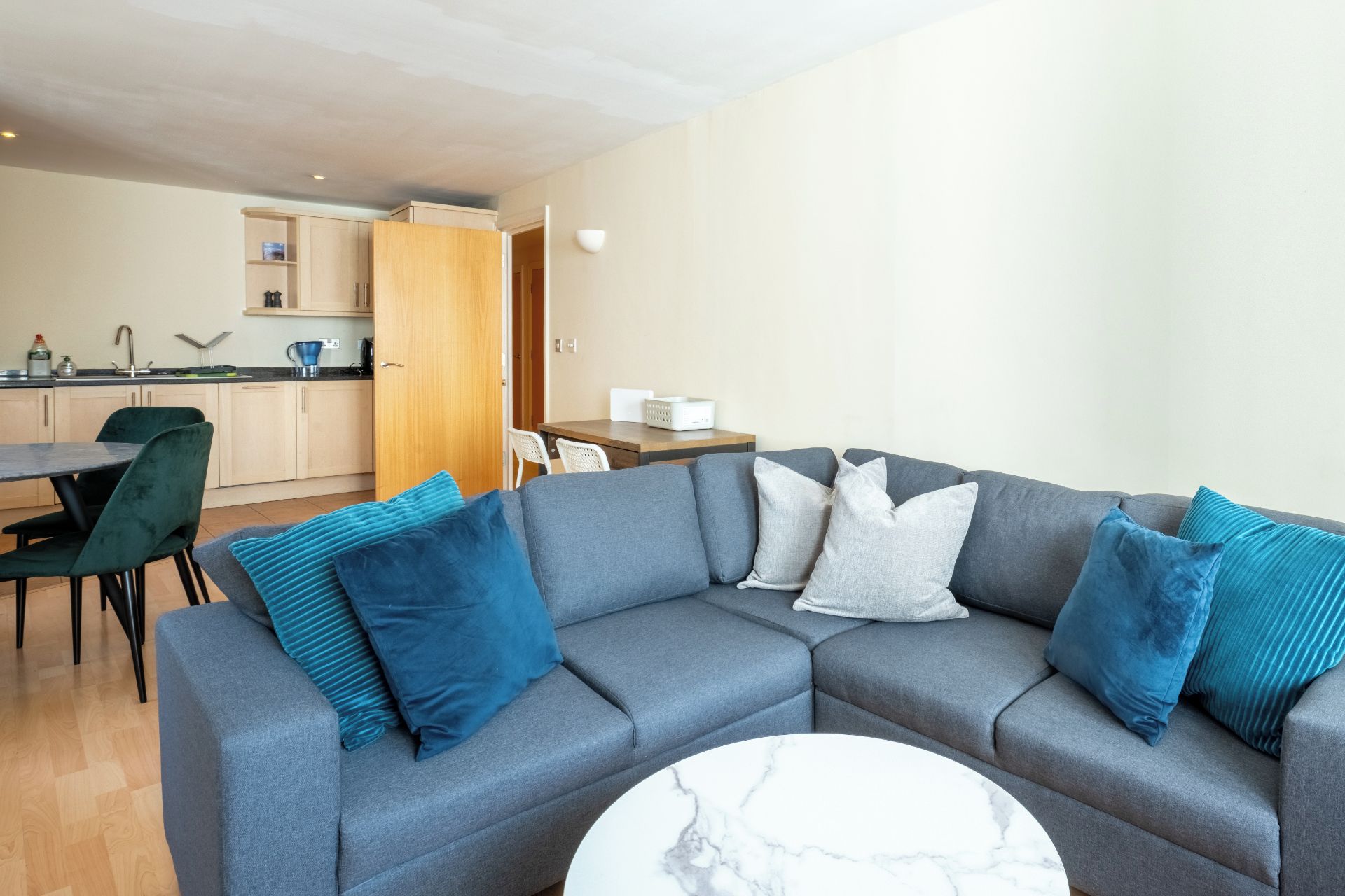 A modern living room with a grey sectional sofa, a round marble coffee table, and a dining area with a wooden table and chairs.