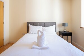 Ein Hotelzimmer mit einem Bett, einem Nachttisch mit Lampe und einem zu einem Schwan geformten Handtuch.