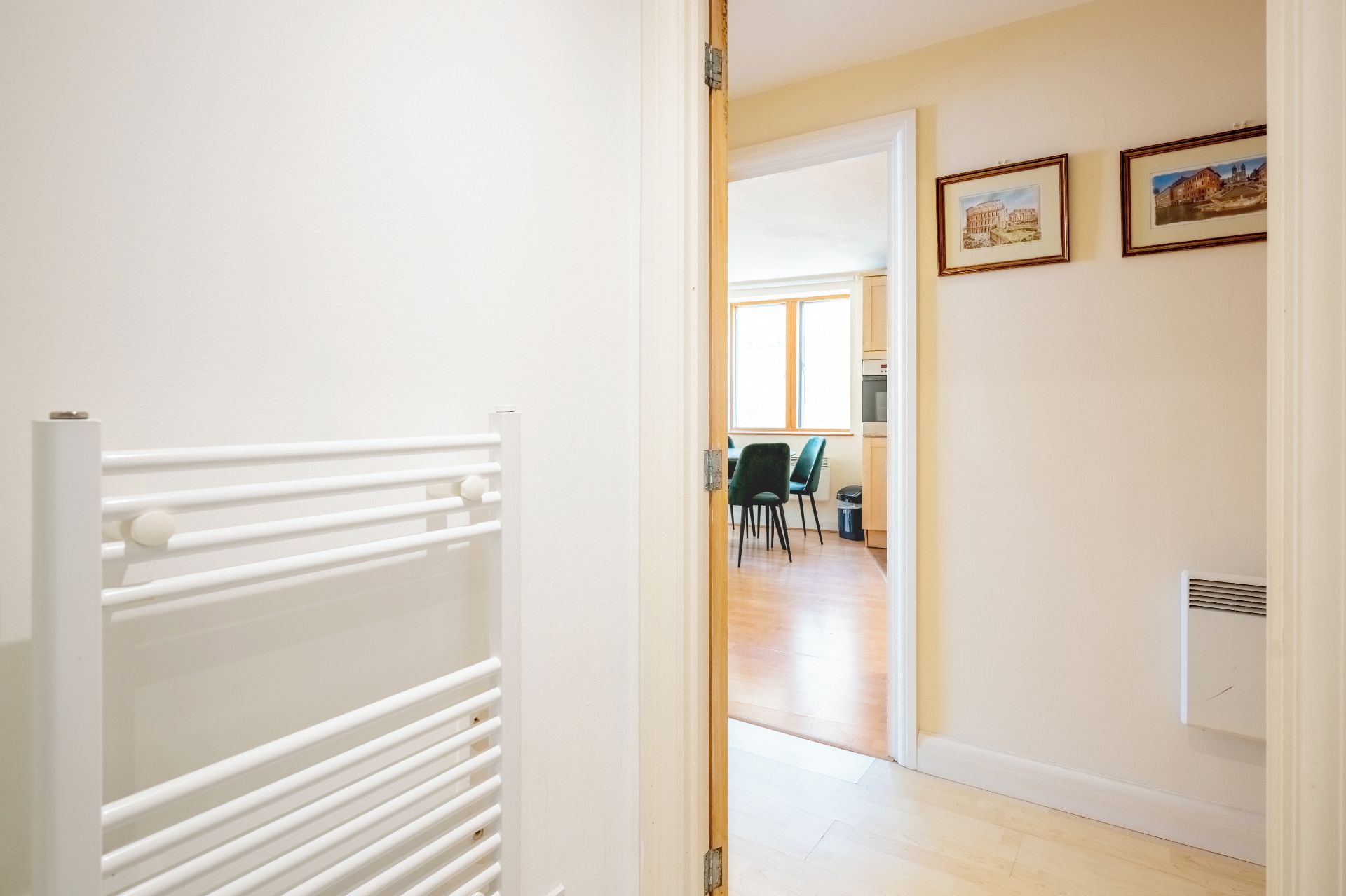 Un couloir menant à une salle à manger, avec un radiateur et des tableaux encadrés accrochés au mur.