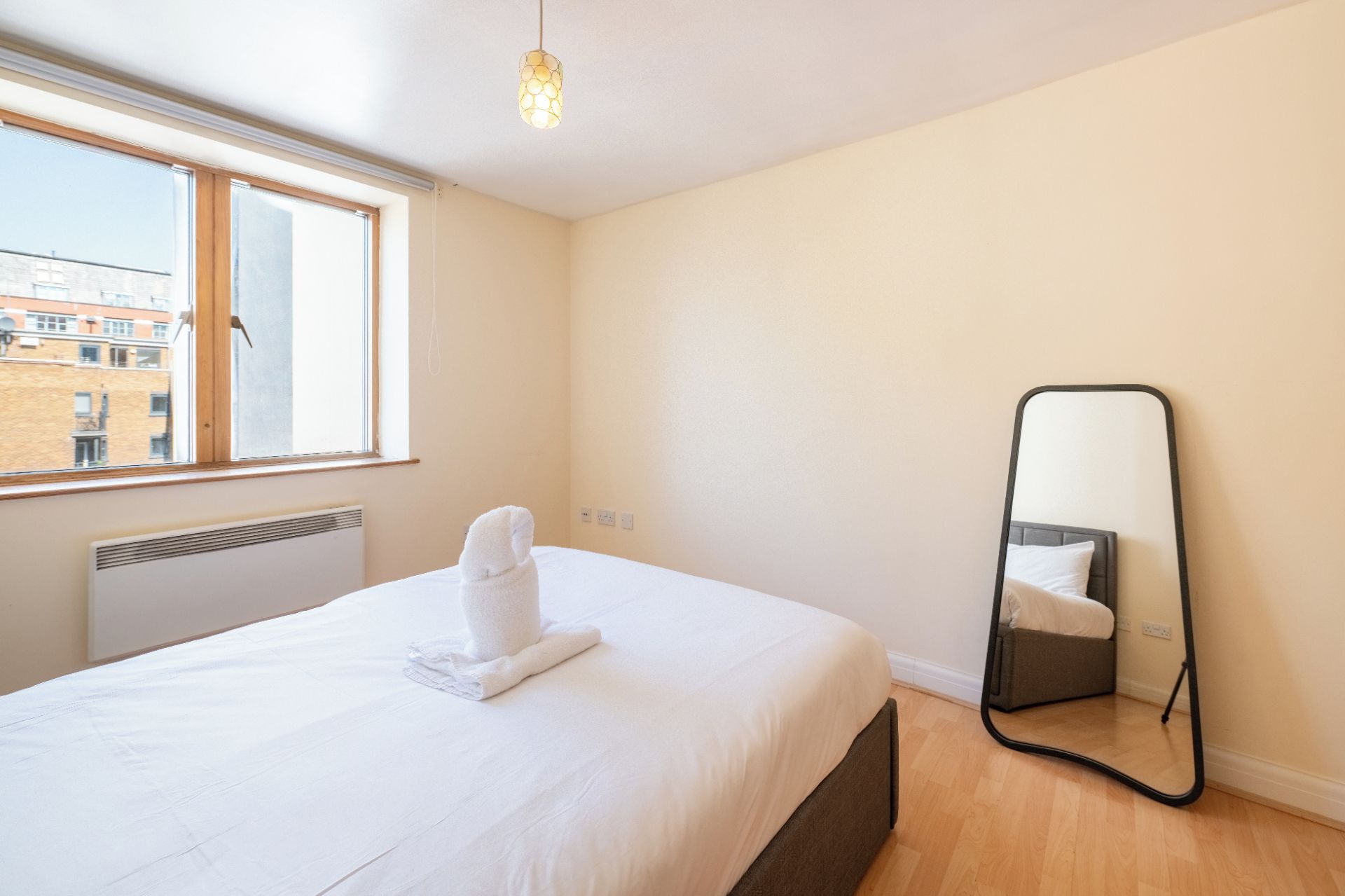 Habitació d'hotel amb llit, finestra, radiador, tovallola i mirall.