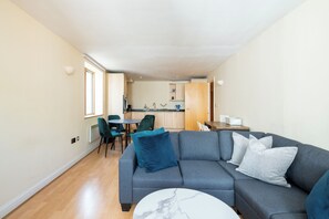 Ein kompakter Wohnraum mit grauem Sofa, rundem Couchtisch und Essbereich mit Stühlen und Tisch.