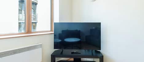 A corner room with a window, a radiator, a black TV stand, and a remote control on it.