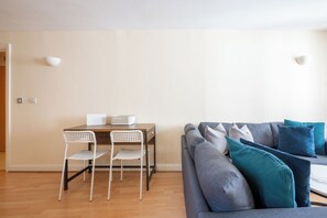 Un salon avec un canapé gris, deux fauteuils blancs, une table en bois et un ordinateur portable.