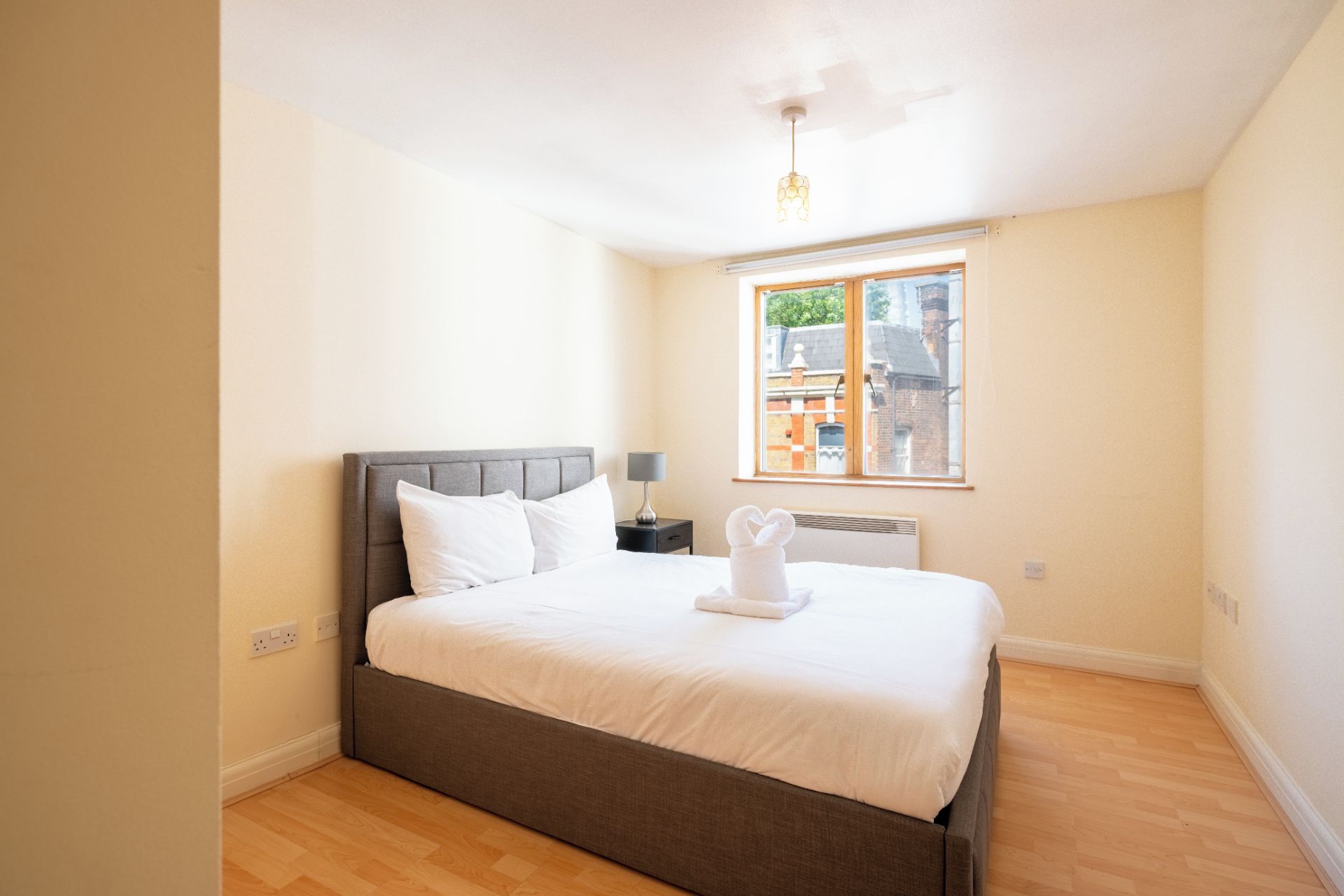 A bedroom with a bed, a nightstand, a lamp, and a window with a view of buildings.