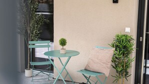 Un petit espace extérieur aménagé avec une table et deux chaises, un pot de fleurs et un mur à motifs.