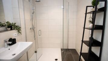 Ein modernes Badezimmer mit einer ein Glasfach raumteilenden Dusche, einem weißen Waschbecken und einer schwarzen Regaleinrichtung mit Pflanzen.