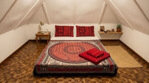 Een knus ingerichte kamer met een bed, nachtkastje, lamp en een klein plankje met decoratieve spullen.