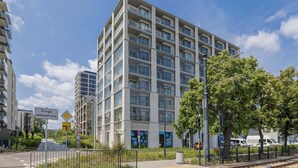 A multi-story residential building with balconies, a pedestrian pathway, and a road with traffic signs. - Bright Apartment with a Balcony | Parking (Warszawa)