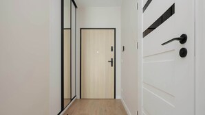 A hallway with a wooden door, a mirror, and a white door with a black handle. - Bright Apartment with a Balcony | Parking (Warszawa)