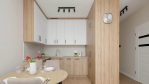 A modern kitchen with white cabinets, a wooden countertop, and a dining area with a round table and chairs. - Bright Apartment with a Balcony | Parking (Warszawa)