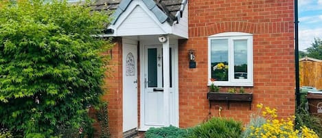 A two-story brick house with a white front door, a small porch, and a visible number '6' on the door.
