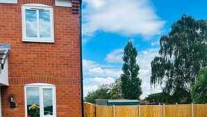 A residential brick house with a driveway, a wooden fence, and a yellow flowering bush. - House Sleeps 4 With Parking and Garden (Newark)
