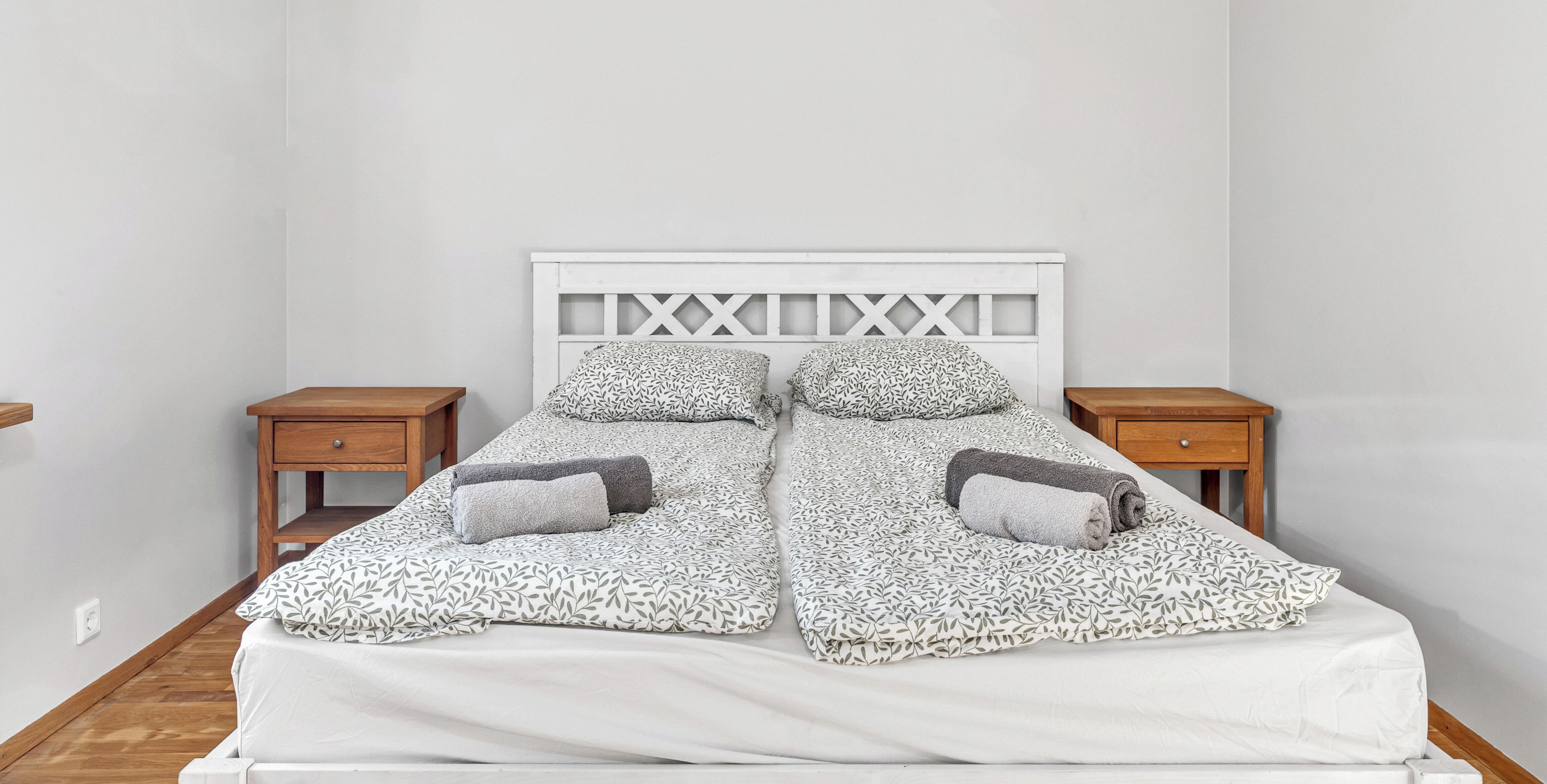 Cama de casal com colcha estampada em folha, dois travesseiros e cabeceira branca com design vazado.