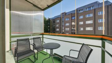 Een balkon met twee stoelen en een tafel, een uitzicht op een meer verdiepingen tellend gebouw, en een vloer van groen kunstgras.