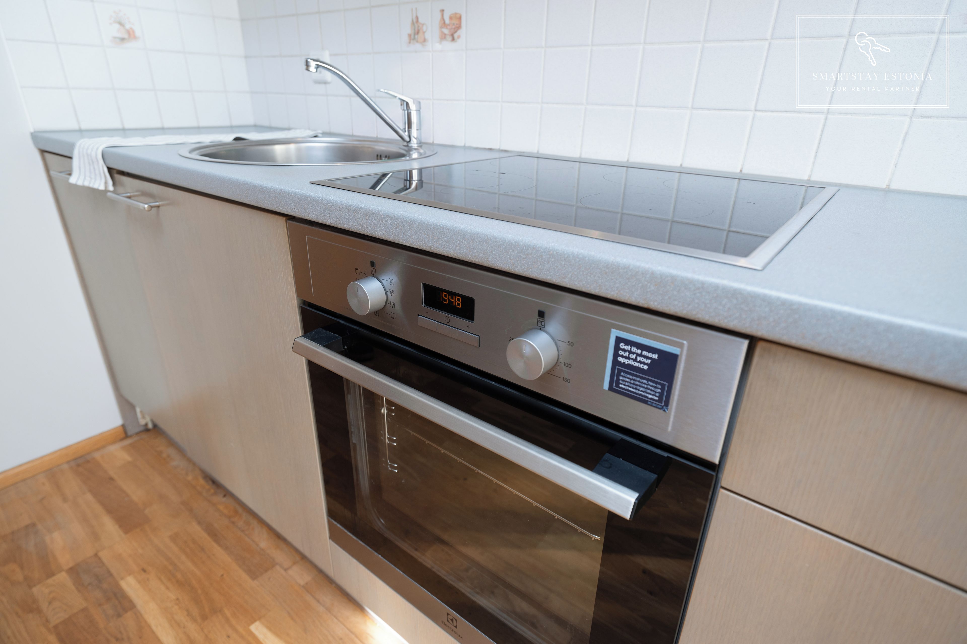 Een keuken met een roestvrijstalen spoelbak, een inbouwoven en een digitale klok die de tijd weergeeft.