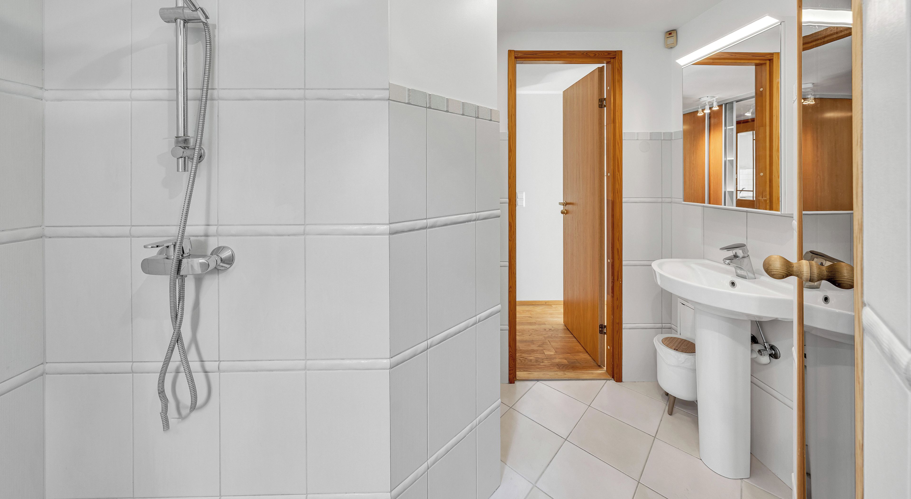 A modern bathroom with a shower, sink, and wooden door.