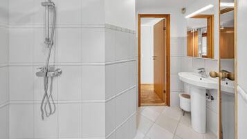 A modern bathroom with a shower, sink, and wooden door.