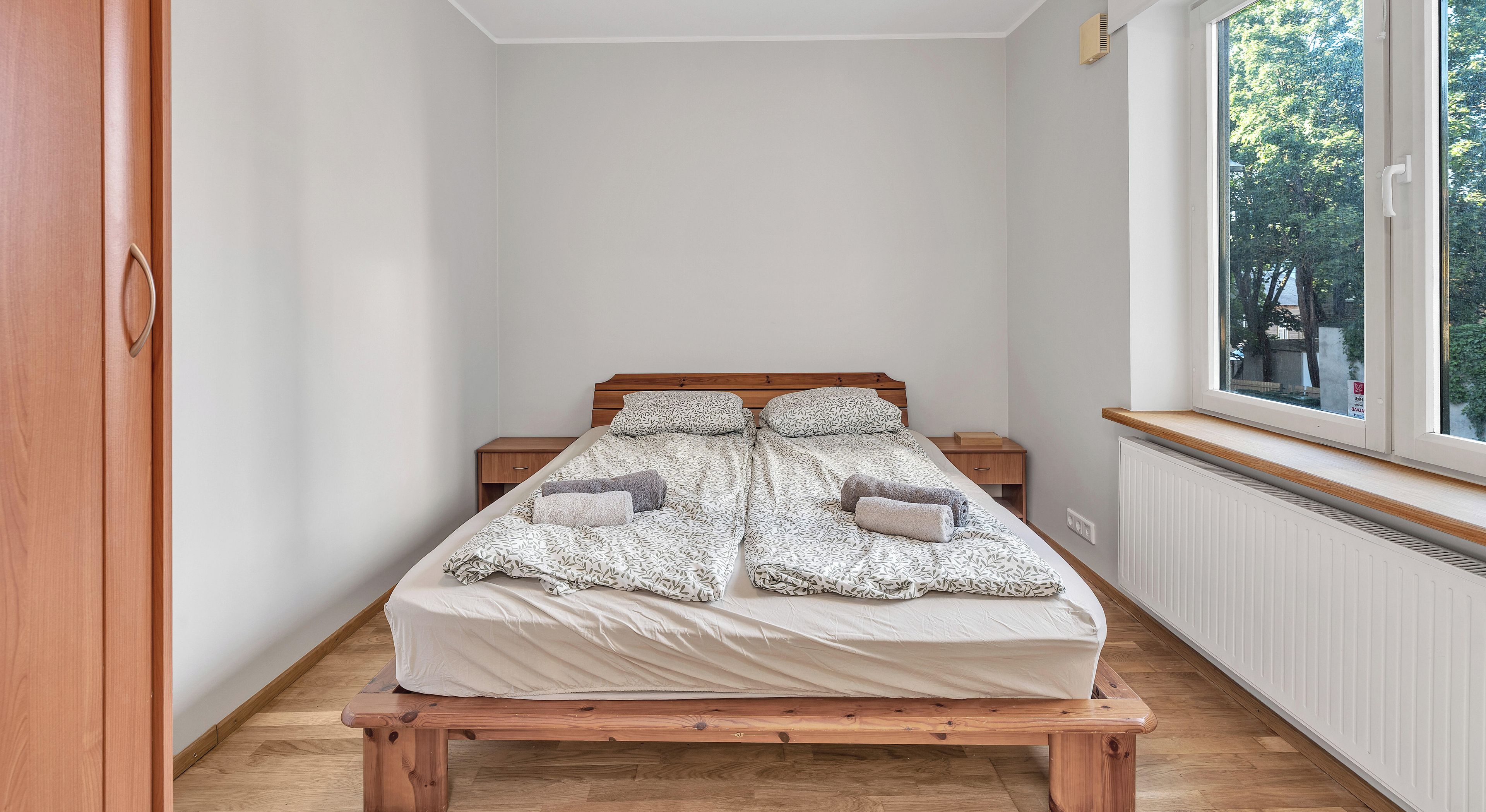 Une chambre à coucher avec un lit, deux tables de chevet, une fenêtre et un radiateur.