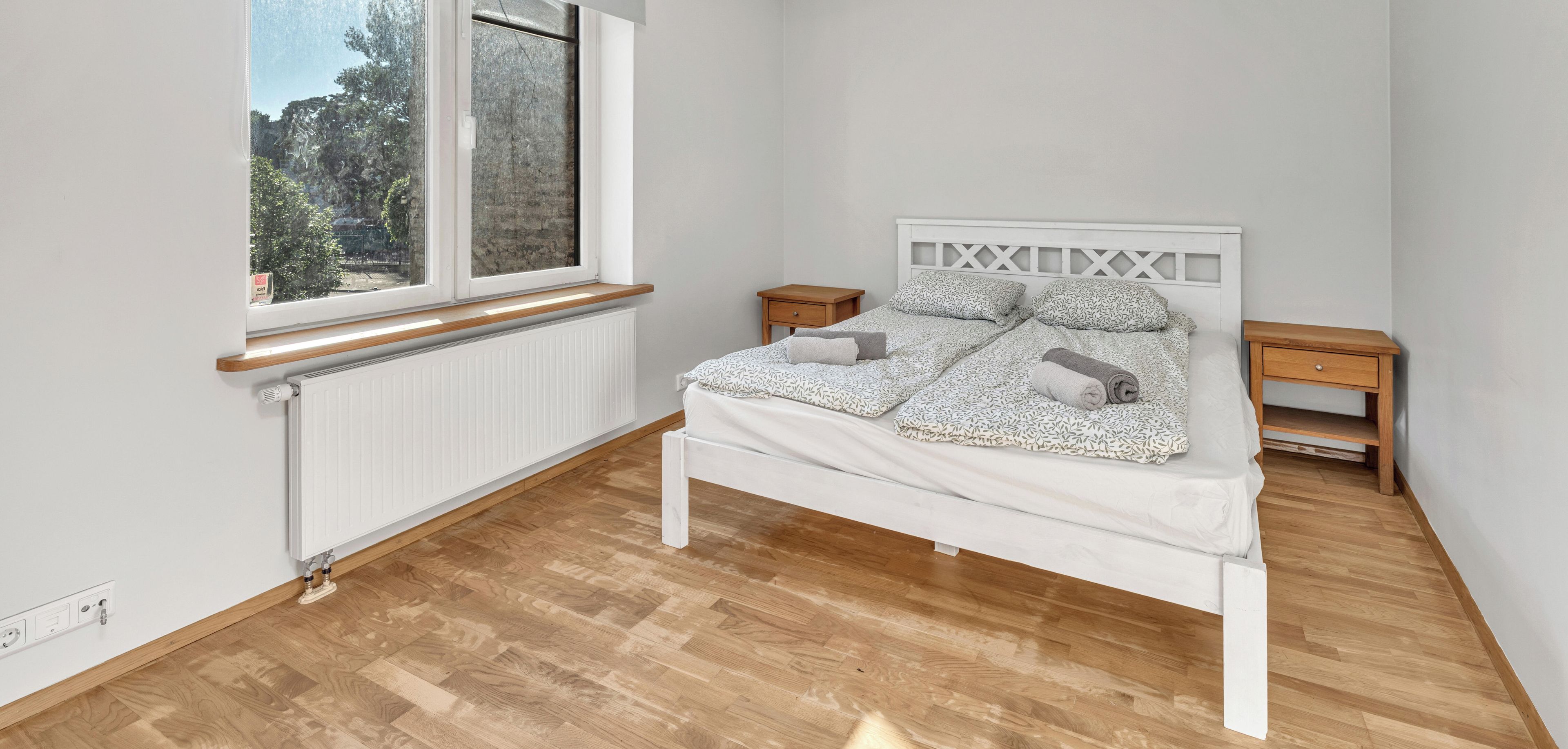 A bedroom with a bed, a window, a radiator, and a wooden floor.