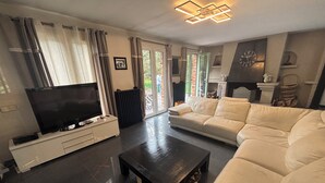 A modern living room with a flat-screen TV, a dark coffee table, a white sofa, and a fireplace. - Beautiful house (Bernay)