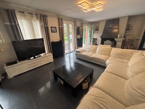 A modern living room with a flat-screen TV, a dark coffee table, a white sofa, and a fireplace. - Beautiful house (Bernay)