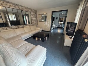 A living room with a sectional sofa, a black coffee table, a TV, and a stone wall. - Beautiful house (Bernay)