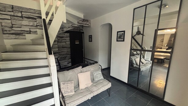 A staircase with stone accents, a sofa with cushions, and a mirrored wall reflecting a dining area. - Beautiful house (Bernay)