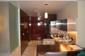 Una cocina moderna con electrodomésticos de acero inoxidable, un comedor con mesa y sillas de madera, y un pasillo con una puerta que da a otra habitación.
