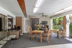 A dining area with a wooden table and chairs, a television, and a view of greenery outside. - Your Search for the Perfect Stay Ends Here! Outdoor Pool, Pets Are Welcome! (Honolulu)
