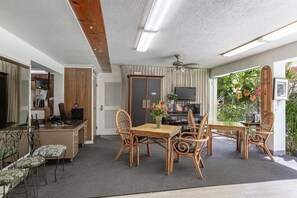 A dining area with a wooden table and chairs, a television, and a view of greenery outside. - The Smart Choice for Your Next Getaway! 2 Units, Outdoor Pool, Pets Allowed! (Honolulu)