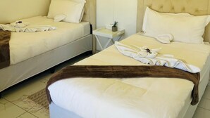 A hotel room with two beds, each with a headboard, a small bedside table, and a potted plant.
