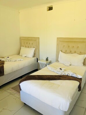 Habitación de hotel con dos camas, cada una con cabecero, mesita de noche y planta en maceta.