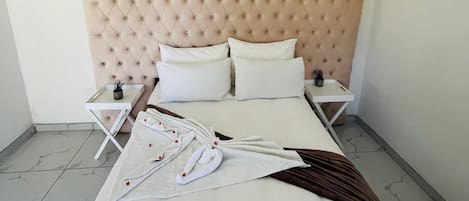 Una habitación de hotel con cabecera capitonada, dos mesitas de noche blancas, cama con ropa blanca y suelo con estampado de mármol.