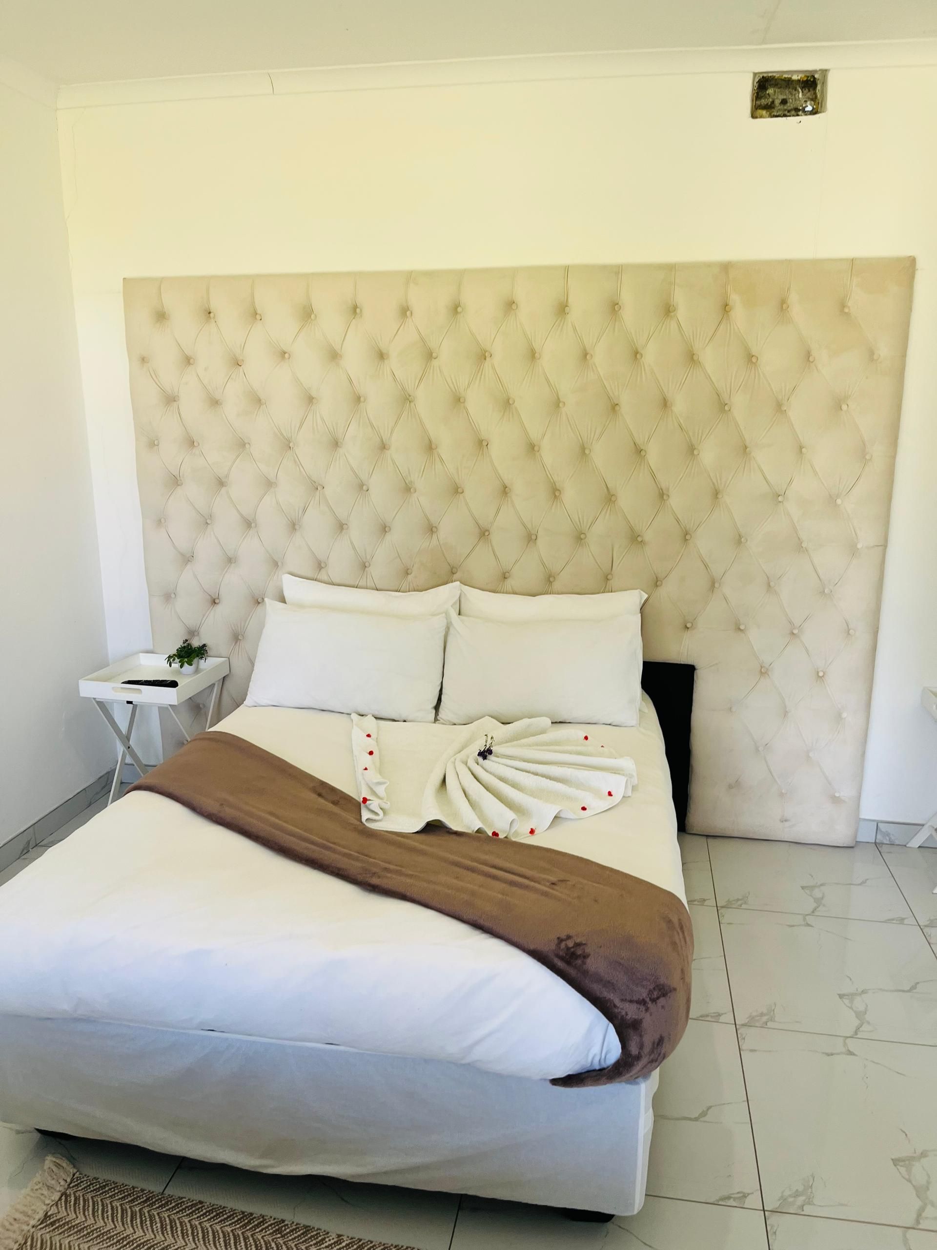 Una cama bien tendida con un cabecero capitonado, ropa de cama blanca y una manta marrón.