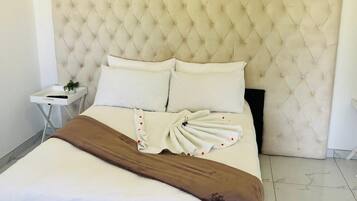 Una cama bien tendida con un cabecero capitonado, ropa de cama blanca y una manta marrón.