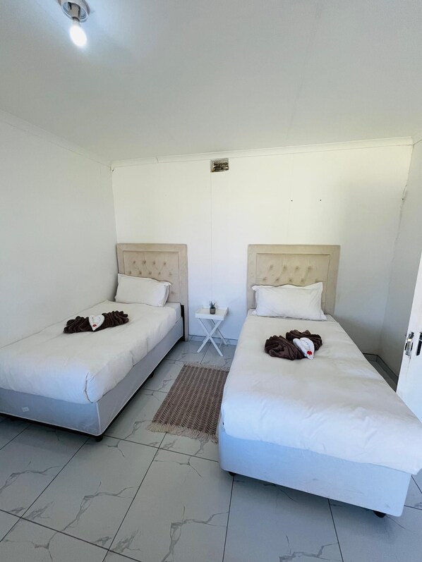 Habitación de hotel con dos camas, una mesita pequeña y una lámpara en el techo.