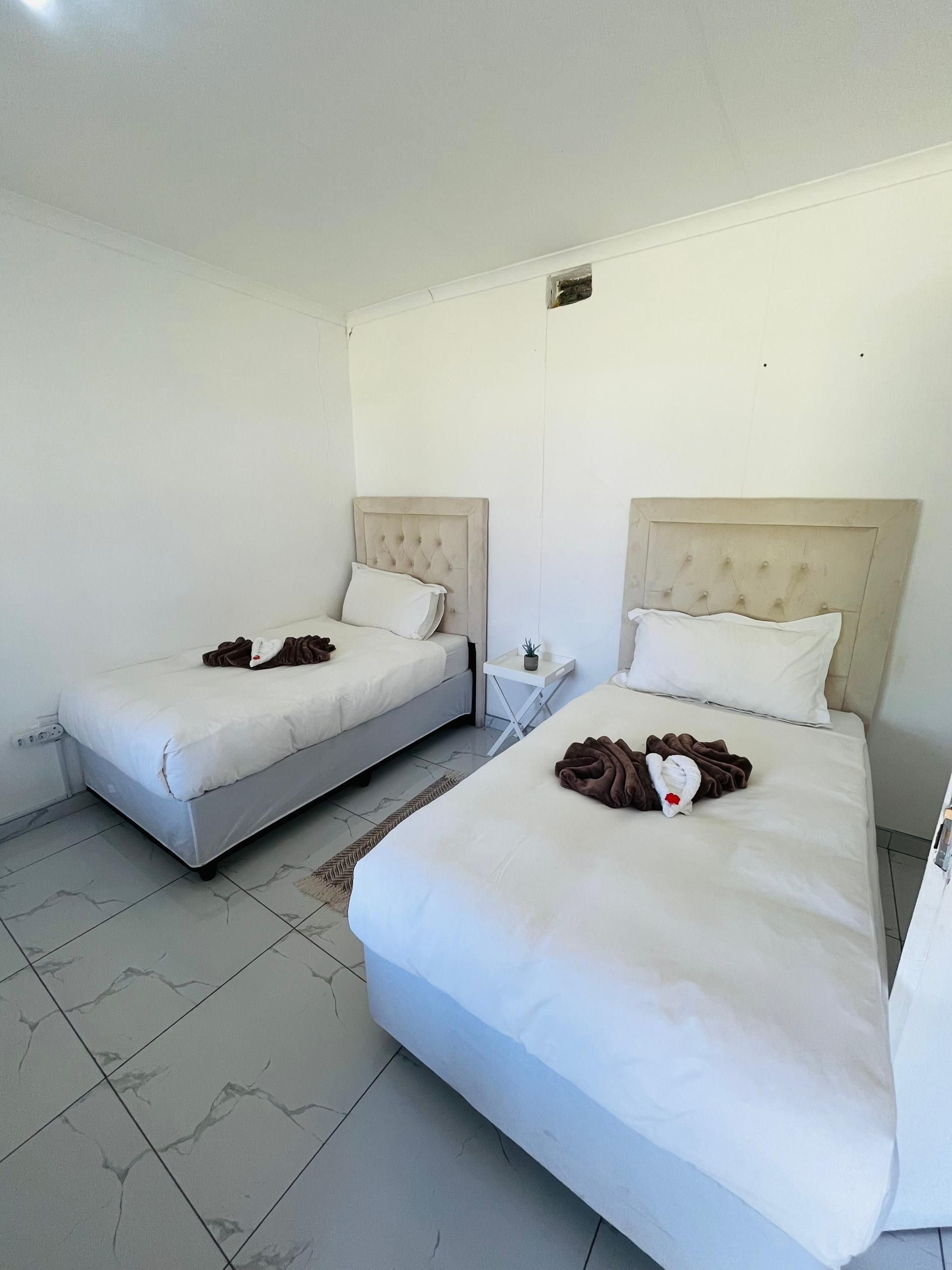 Una habitación de hotel con dos camas, una mesita de noche pequeña y un aplique de pared.