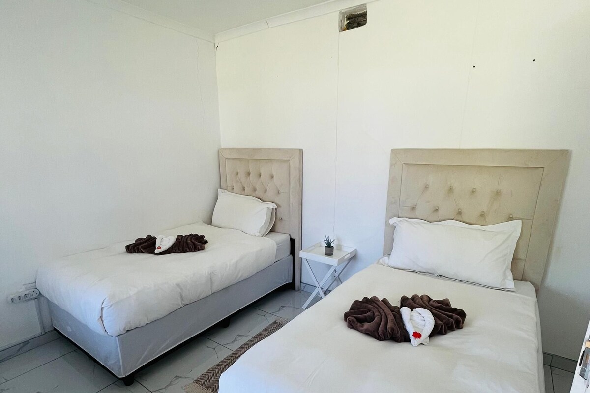 A hotel room with two beds, a small bedside table, and a wall-mounted light fixture.