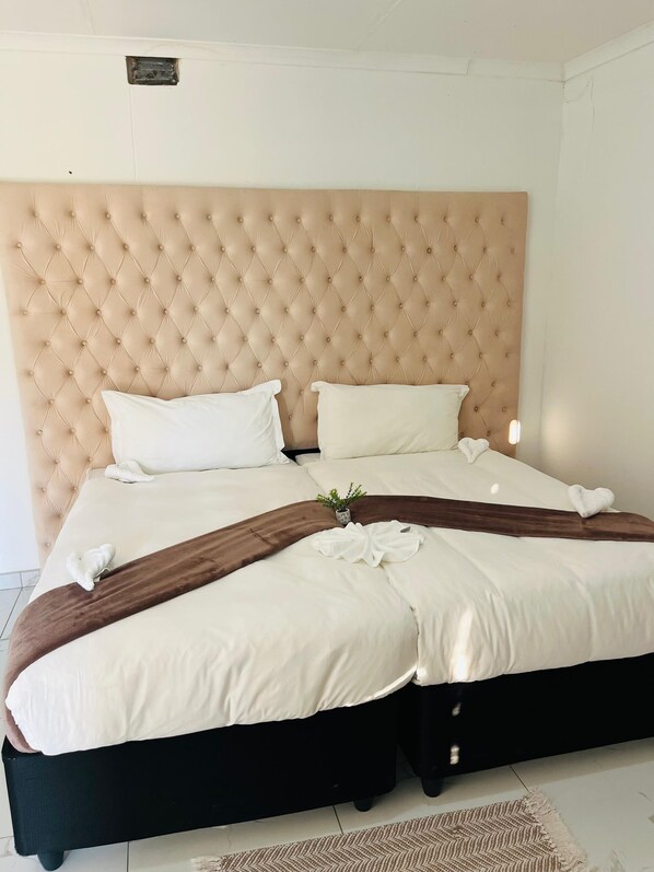 Una cama con cabecera capitonada, ropa de cama blanca y una manta marrón.