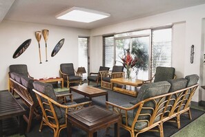 Ein Zimmer mit Korbmöbeln, einem Holztisch und einem großen Fenster mit Jalousien.
