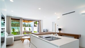 A modern kitchen with a central island, a dining area with a table and chairs, and a large window with a view of greenery. - Villas de Punta Lara 18 by Casasol (Nerja)