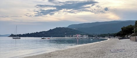 Una playa con barcos, una orilla arenosa y una colina distante.