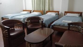 A room with four single beds, two wicker chairs, and a small table.
