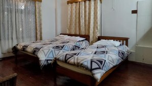 Een hotelkamer met twee bedden, een houten vloer, een plafondventilator en een raam met gordijnen.
